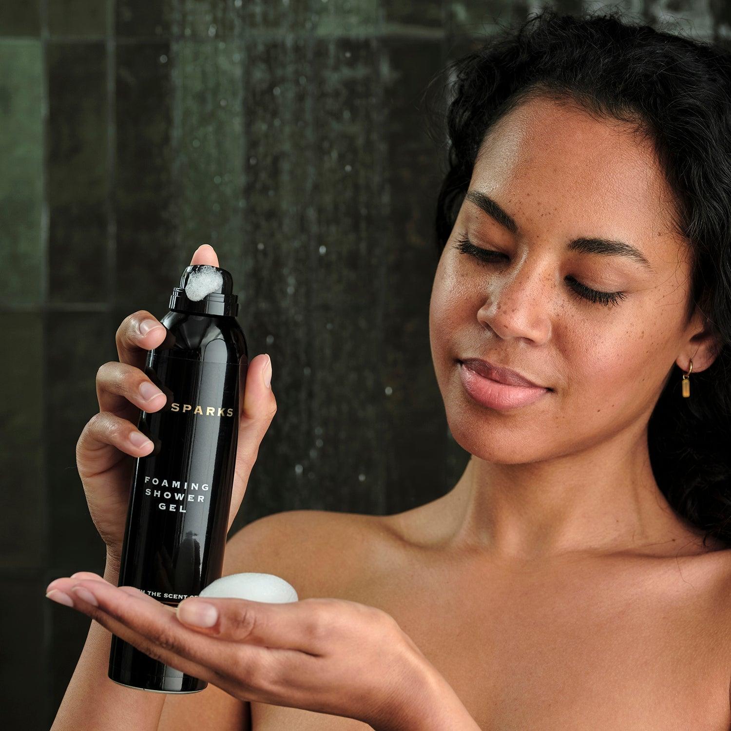 Woman enjoying foaming shower gel, showcasing luxury skincare routine in a modern bathroom.